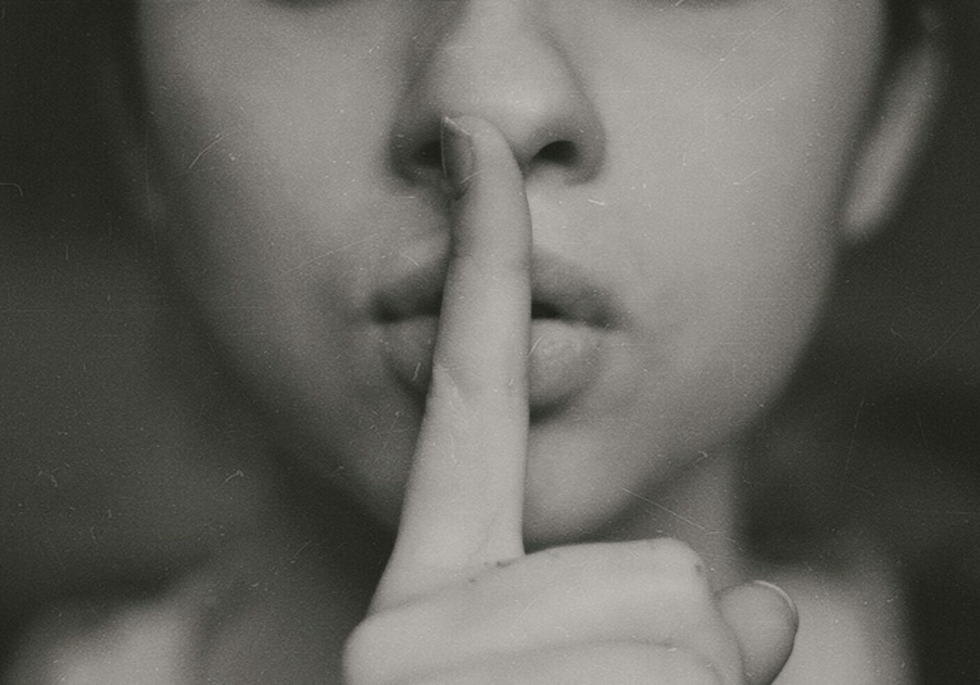 A black and white image of the lover half of a woman's face with her finger against her lips